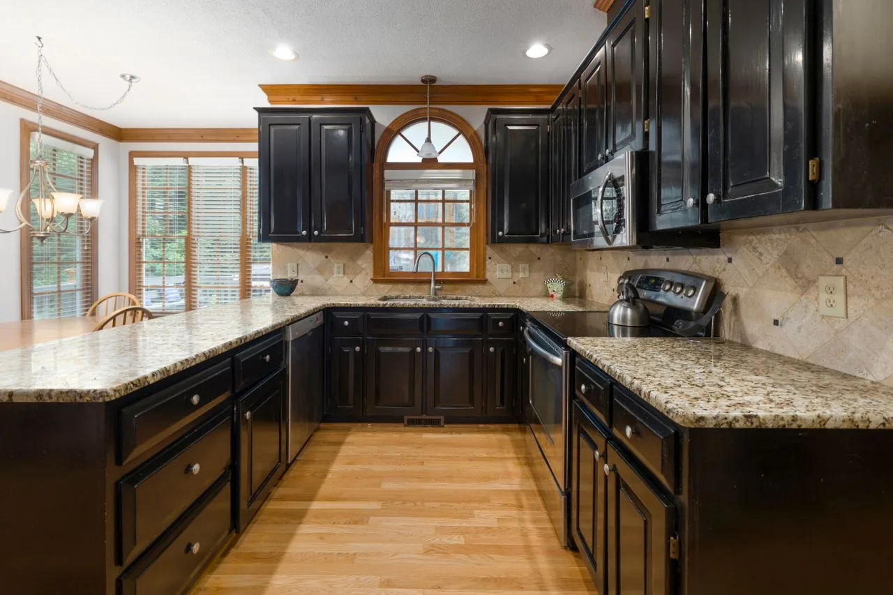 Kitchen with black cabinets, granite counters and warm wood floors
