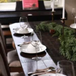Christmas dining table with a cedar greenery runner, brass taper candles and white plates