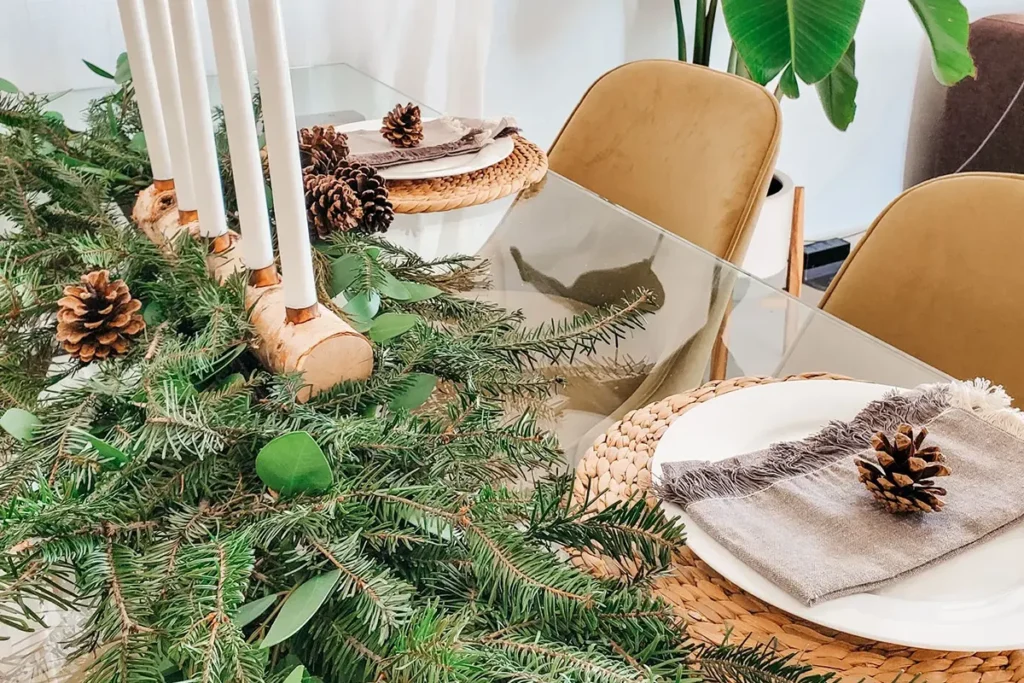 Rustic Christmas dining table with a pine and eucalyptus garland, pinecones and taper candles on a birch log holder