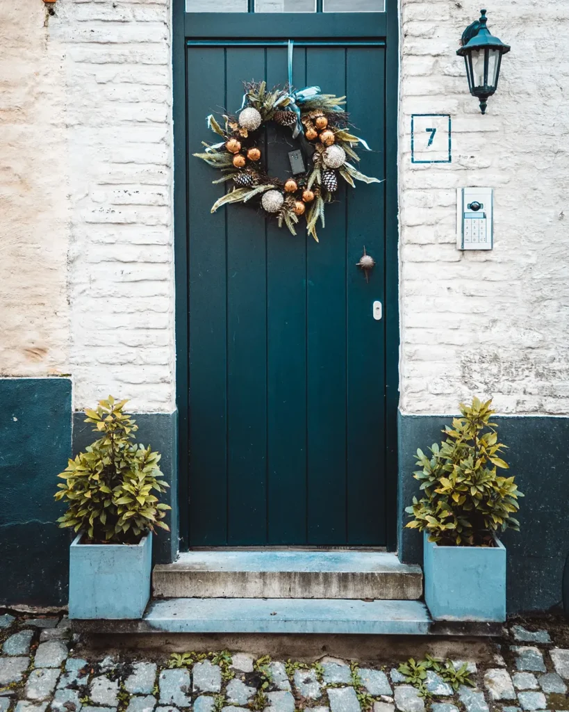 Pair of planters with evergreen shrubs flanking a teal front door with a Christmas wreath