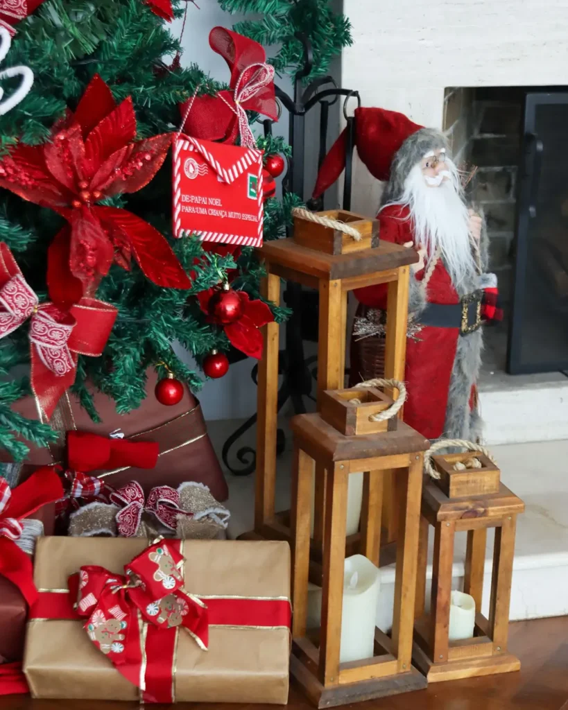 Three wooden lanterns of different heights with LED candles beside a Christmas tree and gifts