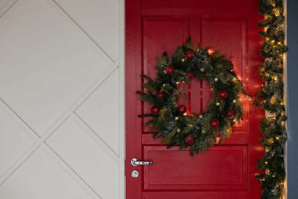 Christmas wreath centered on a red front door, about three-quarters of the door width