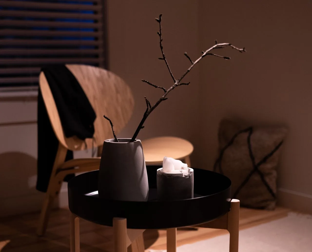 Single branch in a ceramic vase beside a candle in warm, low light