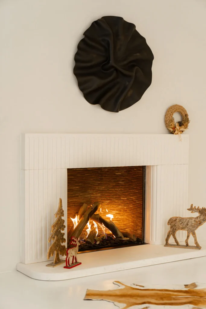 Minimal white Christmas mantel with a lit fire, a small wooden tree and a wooden deer